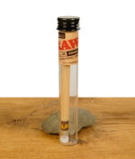 Ein RAW DLX Glass Tipped Cone in einem transparenten Glasröhrchen mit schwarzem Verschluss, auf einem Holzuntergrund platziert.