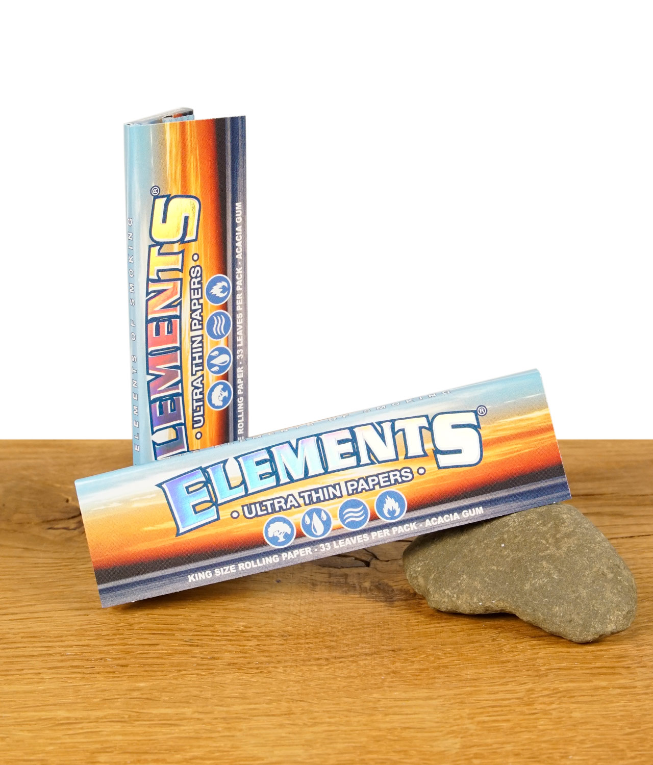 elements-king-size-papers-ultra-thin-jpg Zwei Packungen Elements King Size Ultra Thin Papers auf einem Holztisch, eine liegend und eine stehend, zeigt das farbenfrohe Design der Verpackung.