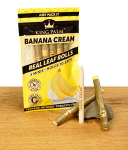 King Palm Banana Cream Packung mit fünf Minis und zwei Blunt Cones auf einem Stein platziert.
