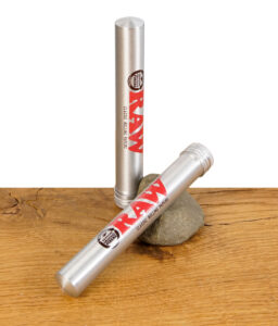 Zwei RAW Aluminium Tubes, eine stehend und eine liegend mit Schraubverschluss, auf Holztisch mit Stein.
