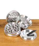 Zerlegter RAW Aluminium Grinder in vier Teilen mit Sieb und Mahlkammer, inklusive Reinigungsbürste, auf Holztisch.