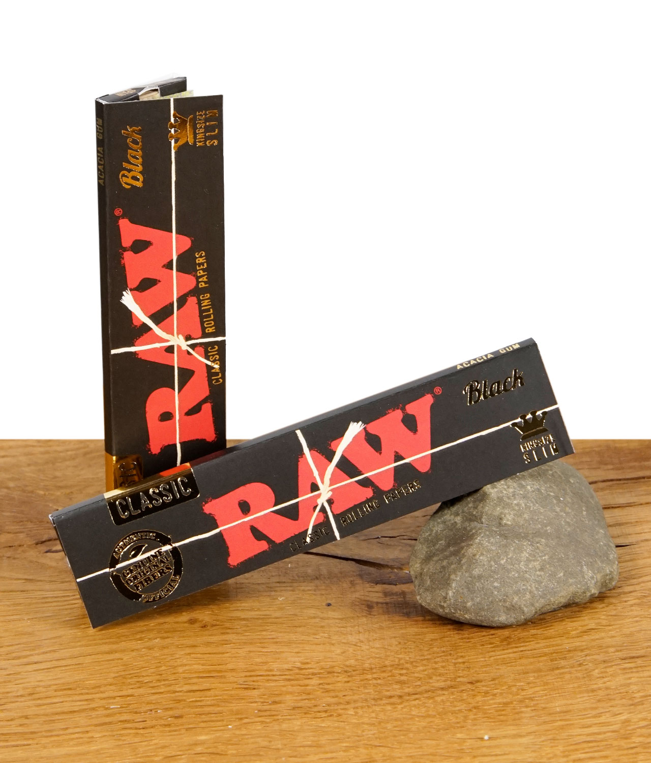 raw-black-king-size-papers-jpg RAW Black Classic Rolling Papers – zwei Packungen ultradünnes, ungebleichtes Zigarettenpapier im schwarzen Design auf Holztisch mit Stein.