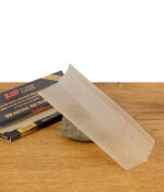 Offenes RAW Black Rolling Paper mit ultradünner Struktur auf einem Stein, Packung im Hintergrund auf Holztisch.