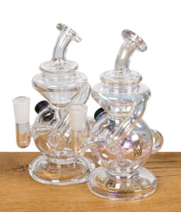 Zwei MJ Arsenal Mini Jig Dab Rigs aus Glas, eine transparente und eine schillernde Variante, nebeneinander auf einem Holztisch platziert.