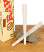 Zwei RAW Organic Hemp Cones King Size aus dem 32er Pack vor der Verpackung auf Naturstein und Holzoberfläche