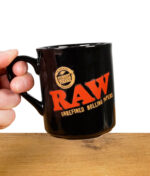 RAW Black Kaffeetasse in der Hand gehalten mit sichtbarem Logo und glänzender Oberfläche