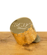 RAW Ethereal Grinder goldfarben, geschlossen, aufrecht geneigt auf Stein – mit RAW-Logo auf dem Deckel