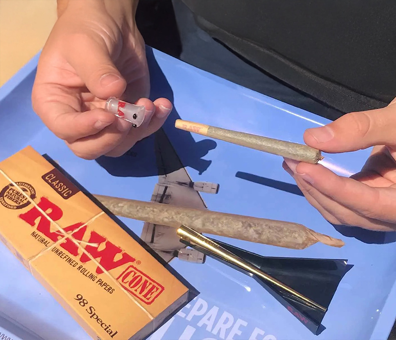 Die RAW 98er Cones auf dem Flying Cone Tray. Person baut Joint mit Glasfilter der Marke RAW Rolling Papers.