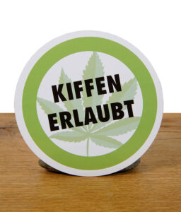 Runder „Kiffen erlaubt“ Aufkleber aufrecht stehend auf Holzuntergrund mit grünem Rand und Hanfblatt