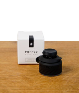 Puffco Peak Pro Joystick Cap in Schwarz (Onyx) neben Verpackung auf Holzuntergrund