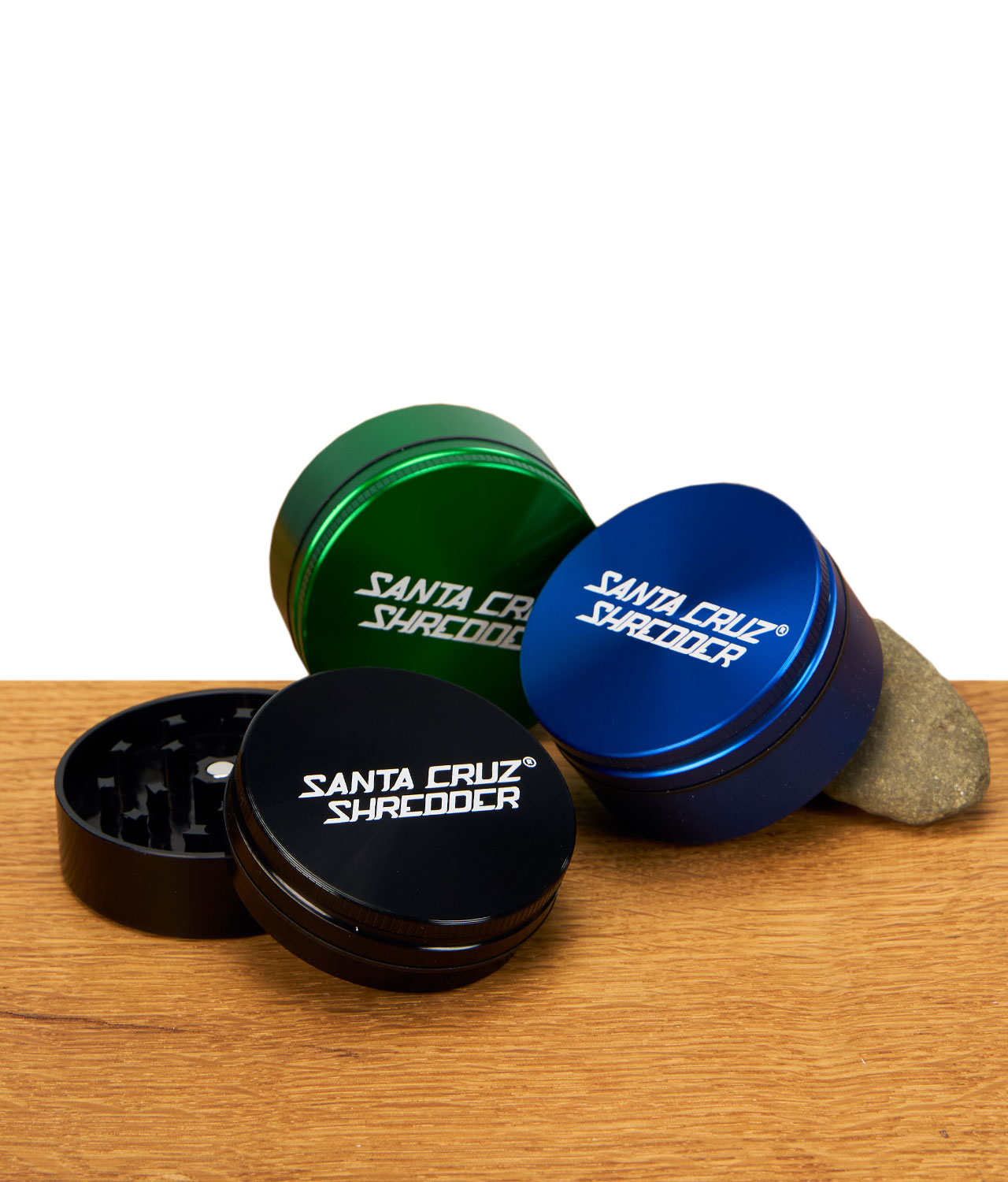 santa-cruz-shredder-2-teilig-53mm-gruppenbild-jpg Drei zweiteilige Santa Cruz Shredder Grinder in Schwarz, Blau und Grün auf Holzuntergrund