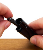 Nahaufnahme der entnehmbaren Zündmechanik eines Clipper Feuerzeugs, gehalten zwischen zwei Fingern.
