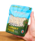 Hand hält den großen 250er-Beutel Weedlez Smart Filter Slim Trino 5 mm mit Sicht auf die Verpackungsgrafik und Filter im Inneren.