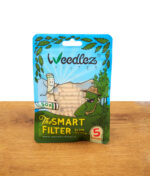 Aufrecht stehender 50er-Beutel Weedlez Smart Filter Slim Trino 5 mm mit blau-grünem Design und transparenter Sichtöffnung auf einem Holztisch.