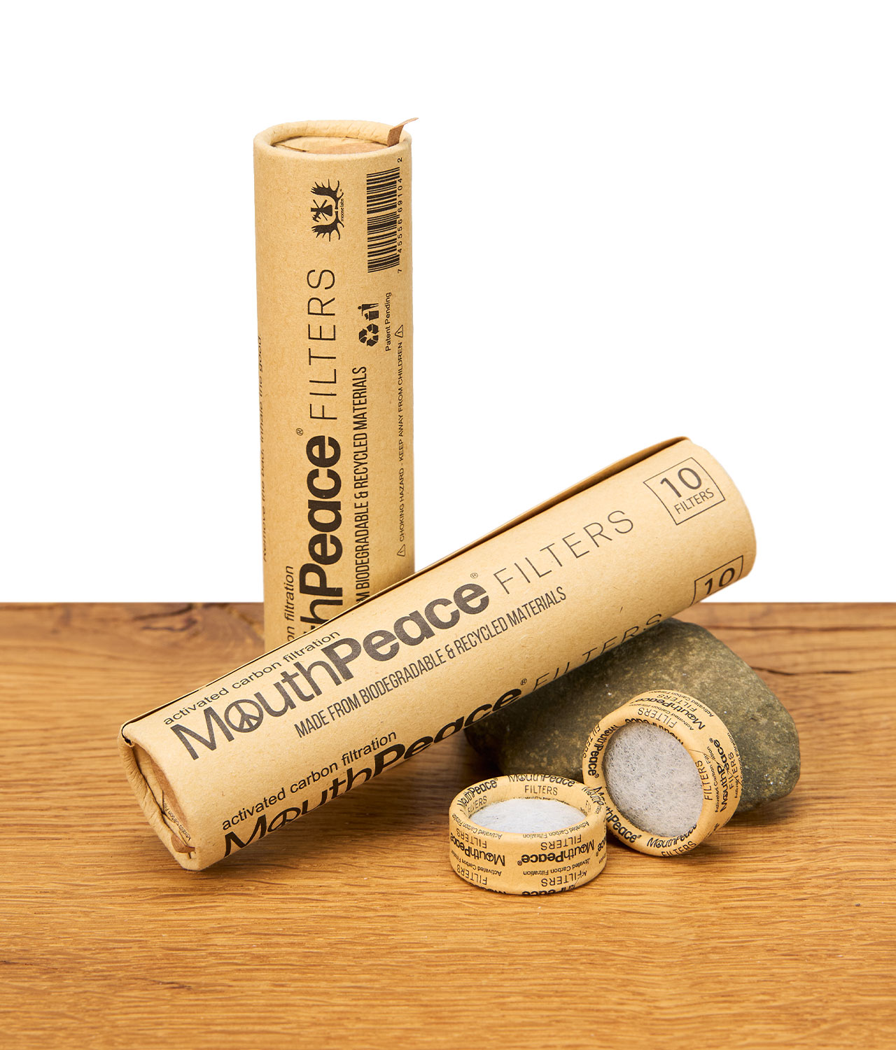 mouthpeace-filters-10er-pack-jpg Verpackung und mehrere MouthPeace Filter liegen dekorativ auf einem Holztisch vor einem Stein.
