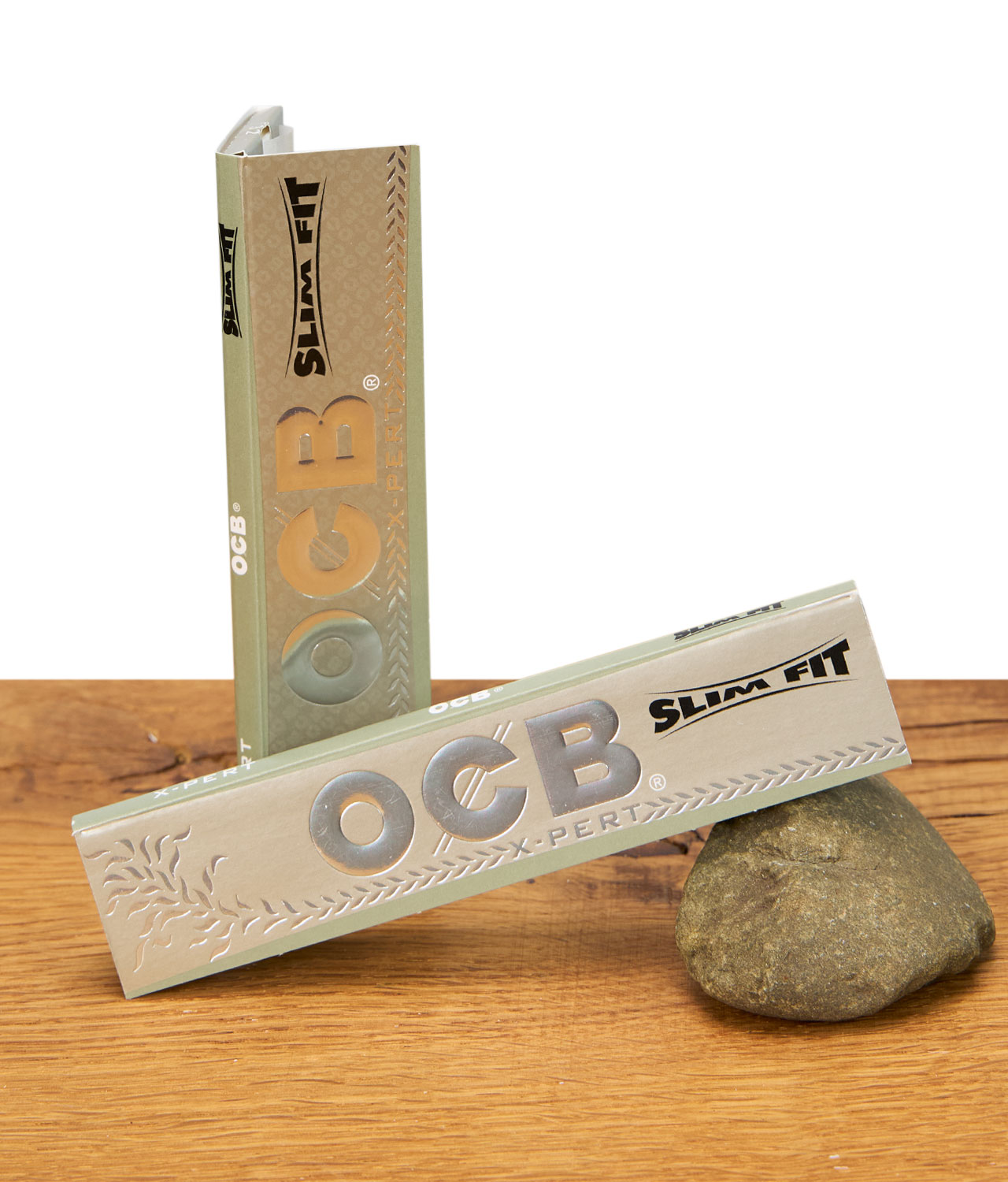 ocb-x-pert-slim-flit-longpapers-jpg Zwei OCB X-PERT Slim Fit Booklets auf Holzuntergrund, eines stehend, eines liegend mit silbernem Logo