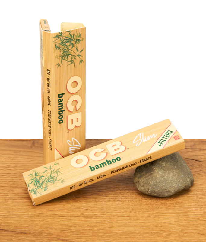Zwei geschlossene OCB Bamboo Slim Packungen mit Bambusdesign auf Holzuntergrund, eine aufrecht stehend und eine liegend.