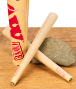 Zwei RAW Classic King Size Cones vor ihrer Verpackung, liegend auf einem Stein und Holzuntergrund