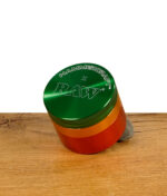Ein Rastafarbender Grinder von RAW und Hammercraft aus Aluminium. Stehend auf Holz.