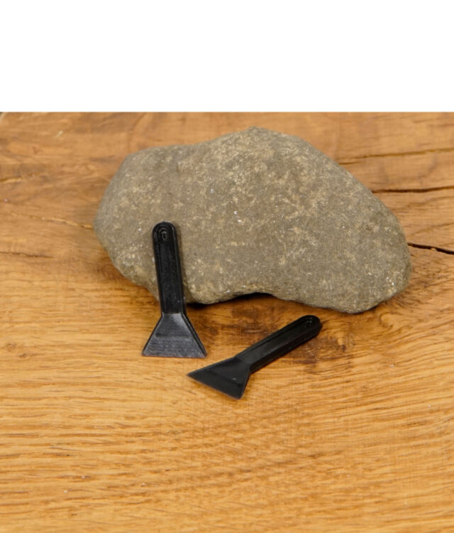 Zwei schwarze Kunststoff-Schaber auf Steinunterlage, ideal zum Auskratzen von Grinder-Resten