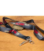 Schwarzes Schlüsselband mit RAW Black Logo und Metallclip auf Holzuntergrund.