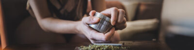 grinder klemmt und frau versucht diesen zu öffnen. Darunter liegt ein Joint bereit