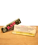 RAW Ethereal Classic Rolling Papers, Packung geöffnet mit Papier und Beschreibungstext sichtbar, goldenes Design auf Holzuntergrund.