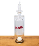 RAW Gravity Cone aus Glas mit Logo, Pingpong-Ball im Inneren, stehend auf Holztisch, Studioaufnahme.