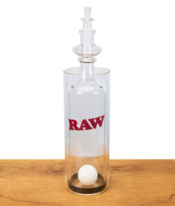 RAW Gravity Cone aus Glas mit Logo, Pingpong-Ball im Inneren, stehend auf Holztisch, Studioaufnahme.