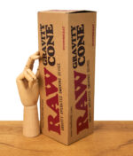 Verpackung des RAW Gravity Cone mit großem Schriftzug, neben einer Holz-Hand auf Holztisch, Produktfoto.
