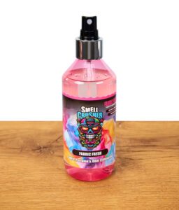 Smell Crusher Fabric Fresh Textilparfüm und Geruchsentferner, pinke Sprühflasche mit buntem Etikett stehend auf Holztisch, freigestellt.
