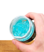 Hand hält geöffneten Smell Crusher 40 Day Gel Lufterfrischer, Blick auf blaues Gel im Glasbehälter, Nahaufnahme.
