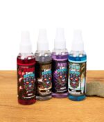 Vier verschiedene Smell Crusher Perfume Lufterfrischer Sprays in den Sorten Cherry, Black, Lavender und Breeze, stehend auf Holztisch mit Steinen.