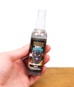 Hand hält Smell Crusher Perfume Black Lufterfrischer Spray mit markantem Totenkopf-Etikett, Produktfoto vor weißem Hintergrund.
