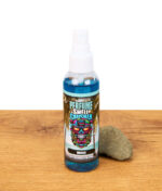Smell Crusher Perfume Breeze Lufterfrischer Spray in blauer Flasche mit Palmenmotiv, platziert auf Holztisch mit Stein.