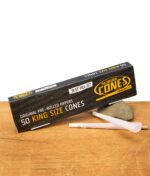 Zwei The Original Cones King Size vorgedrehte Papers vor schwarzer Box auf Stein und Holztisch, perfekte Joints in Sekunden