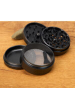Schwarzer Black Leaf Lotus Grinder 63mm geöffnet und zerlegt mit Sicht auf Sieb und Mahlwerk, auf Holztisch