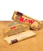 RAW Classic Ein Viertel Size Papers geöffnet auf Holzuntergrund, einzelne Blattpackung und Packung sichtbar, vegan und ungebleicht – ideale Blättchen für selbstgedrehte Zigaretten