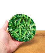 Hand hält Fire Flow Aschenbecher mit buntem Hanfblatt-Design, kleiner runder Metallaschenbecher als Cannabis Accessoire