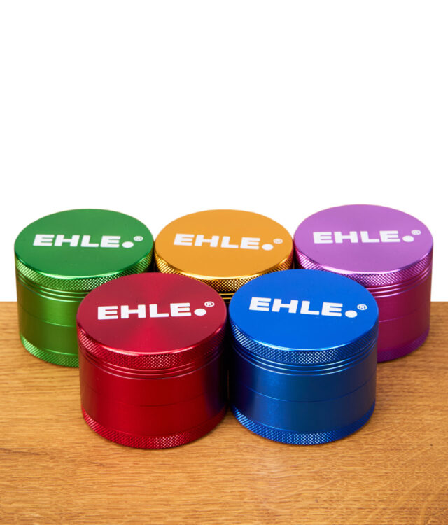 Fünf bunte EHLE Aluminium Grinder (grün, rot, orange, blau, lila) mit Logo nebeneinander stehend auf Holztisch.
