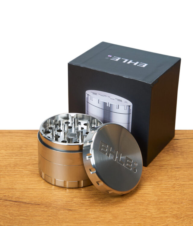 EHLE Edelstahl Grinder geöffnet vor schwarzer Verpackung mit Produktabbildung, auf Holztisch.