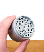Silberner EHLE Keramik Grinder wird mit der Hand gehalten, Fokus auf Mahleinheit über Holztisch.