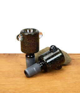 Zwei Glasköpfe aus Schwarzglas mit Glitzer, einer stehend und einer liegend auf Holztisch mit Stein – Ersatzköpfe für Bong, stilvolles Glaszubehör mit Glitzereffekt.