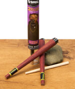 G-Rollz Blunt Cones Strawberry Cheesecake King Size, zwei lila Cones, Stopfhilfe und Verpackung auf Holz.