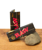 RAW Black Classic Rolling Papers 1 1/4 Size, schwarze Verpackung mit rotem Logo, auf Holzuntergrund.