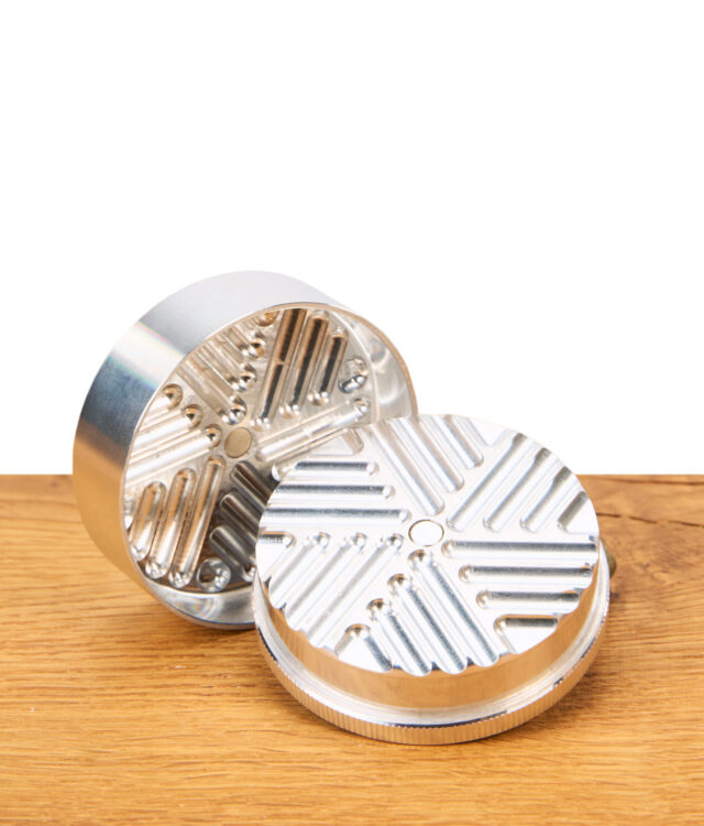 Silberner Grinder aus Aluminium ohne Zähne liegt offen auf Holz