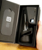 Puffco New Peak Vaporizer in Schwarz in geöffneter Verpackung mit Zubehör, gehalten in einer Hand.