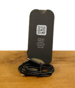 Puffco New Peak Ladekabel in Schwarz mit QR-Code-Karte auf Holz mit Stein im Hintergrund.