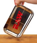 RAW Rolling Tray in silberner Metallic Optik auf einem Holzbrett, schräg von einer Hand gehalten