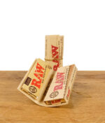 RAW Classic Connoisseur 1 1/4 Papers mit vorgerollten Tips aufgefächert auf Holztisch – praktische Kombipackung ungebleichter Blättchen für perfekte Joints bei buyhigh.